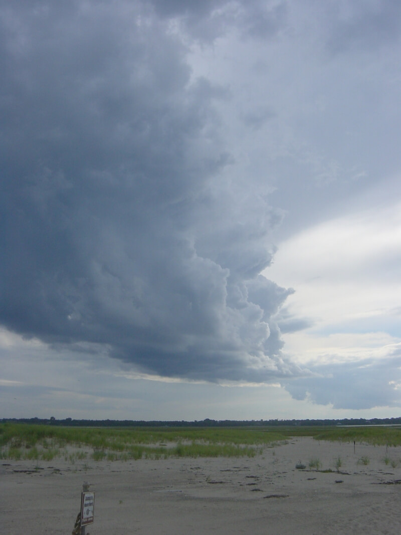 A photograph of building cumulus clouds along a Cape Cod beach.